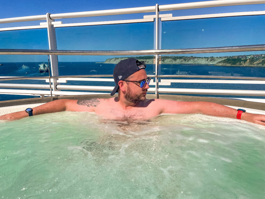 Man wearing a baseball cap and sunglasses in a hot tub on the deck of Sky Princess Princess Cruises
