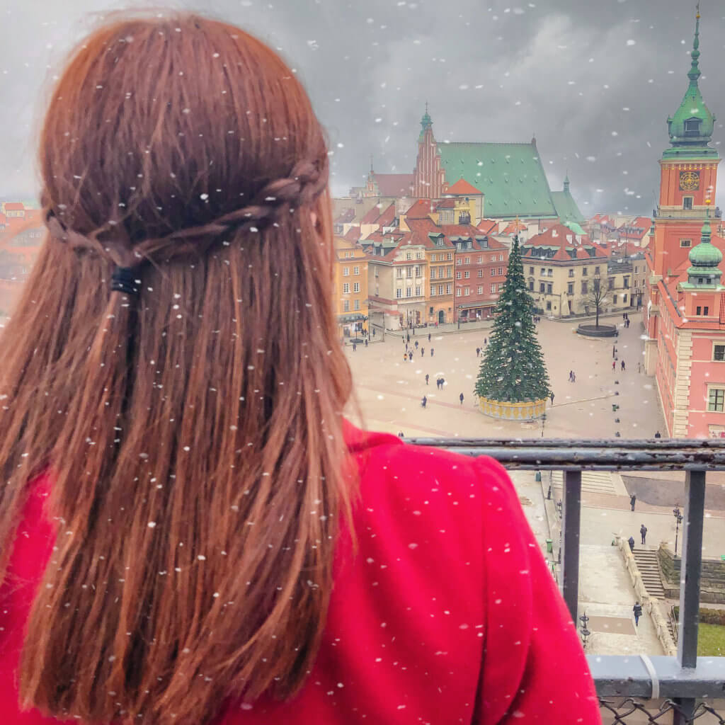 Woman looking at the christmas tree outside Warsaw Castle while it is snowing.
