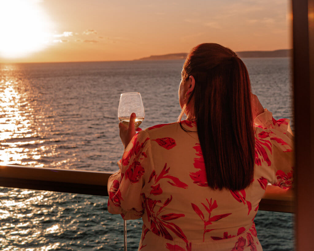Woman drinking a glass of wine at sunset on her first cruise.