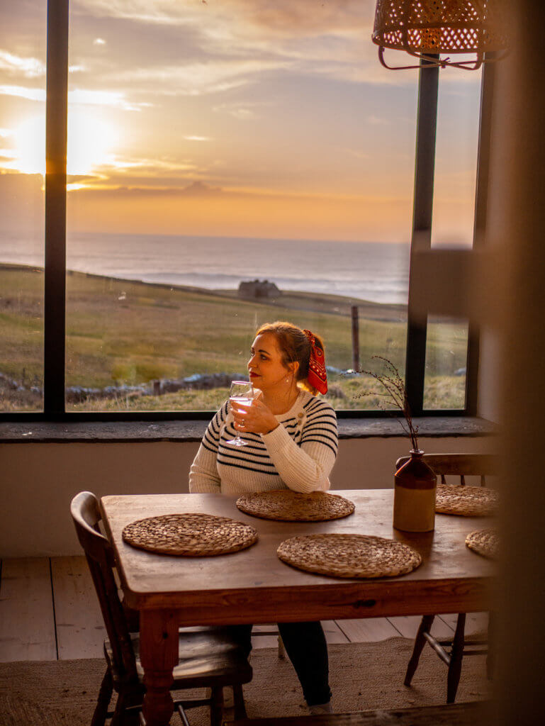 Woman sitting at the kitchen table in Russells Cottage in Doolin Ireland at sunset