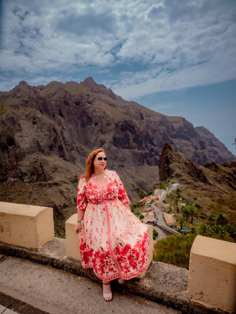 Woman in a red dress sitting on a wall overlooking the village of Masca in Tenerife one of the best places to visit on a Tenerife road trip.