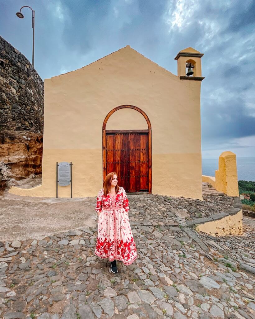 Woman in a red dress standing in front of a yellow church called Hermitage of San Pedro in Tenerife