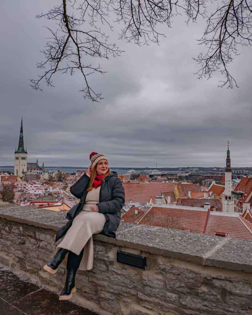 Woman sitting on a wall overlooking elevated views of Tallinn old town at Kohtuotsa viewing platform