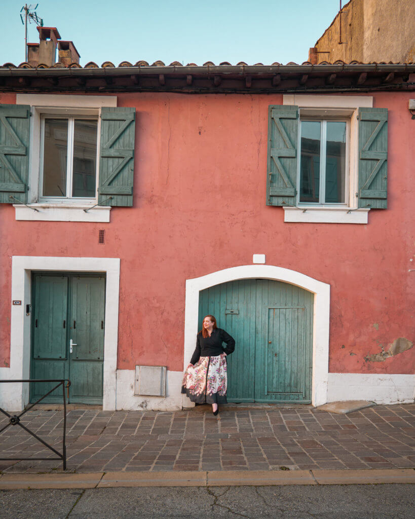 Woman in a long floral dress leaning against a pink house in Carcassonne France