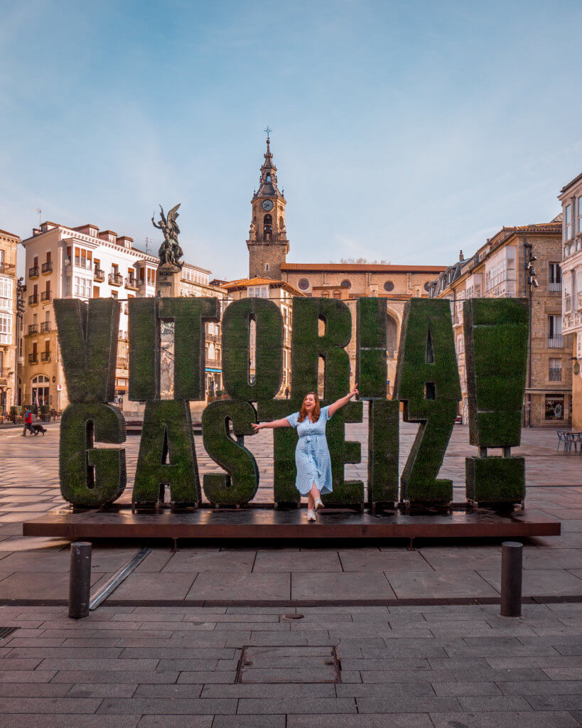 Nicola Lavin, Irish Travel Blogger stands in front of the famous Vitoria-Gastiez sign made out of grass.