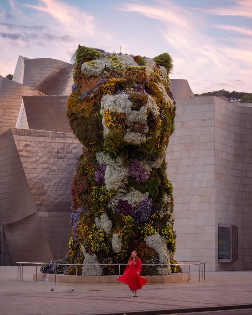 Nicola wearing a red dress twirls in front of Jeff Koons Puppy in Bilbao Spain