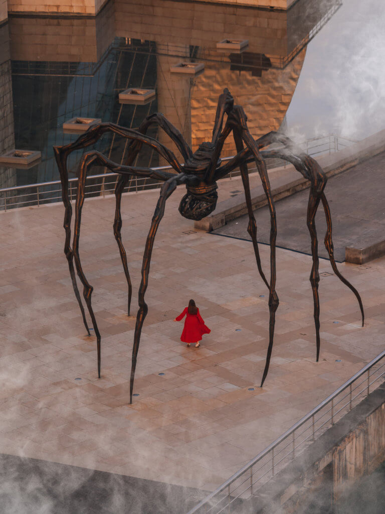 Woman wearing a red dress standing under Maman sculpture in Bilbao Spain