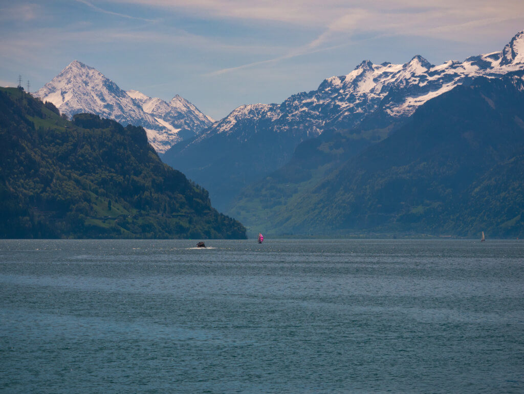 Pink sailboat on Lake Lucerne surrounded by snow-capped mountains.