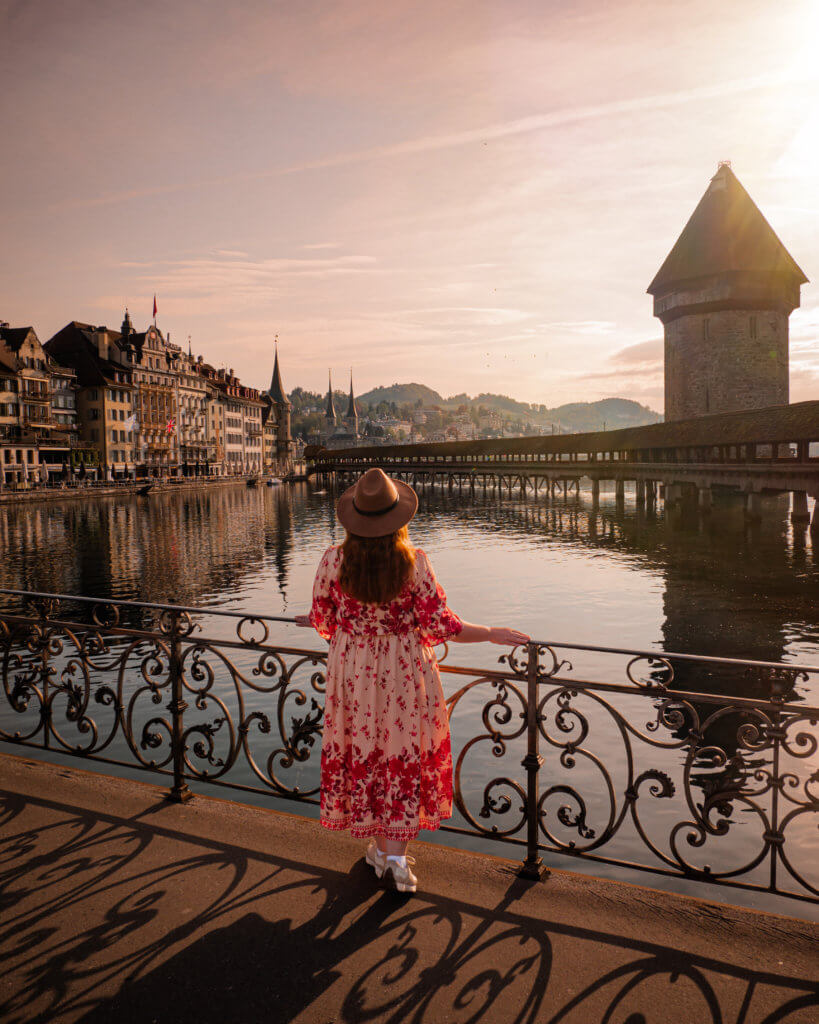Nicola Lavin Travel Blogger stands on a bridge in Lucerne Switzerland and looks at the architecture of Lucerne Old Town