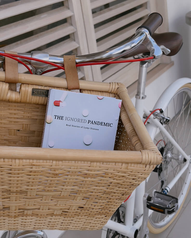 Bicycle with a book in the basket. The book is titled ignored pandemic: real stories of lyme disease