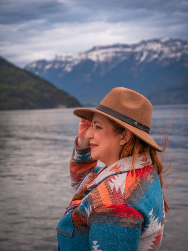 Nicola Lavin wearing a hat and an aztec jacket looking at the water of Lake Thun