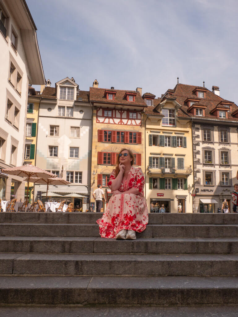 Nicola Lavin, travel blogger, sits on the steps of Kornmarkt in Lucerne Old Town during one day in Lucerne.