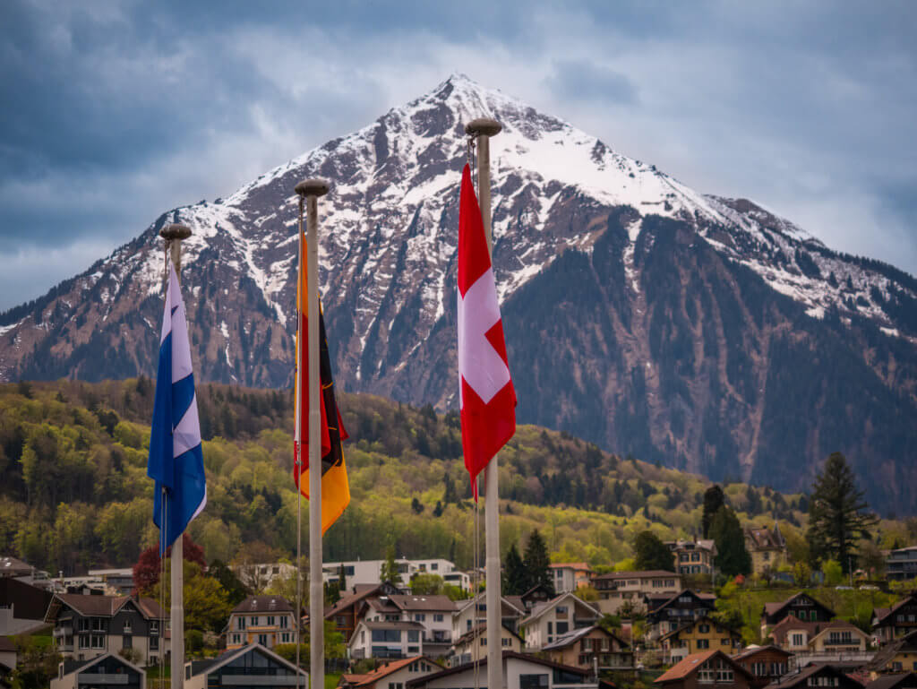 Three swiss flags in the foreground of a dramatic swiss landscape
