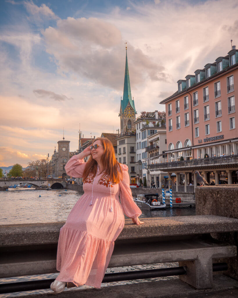 Nicola wearing a pink dress sits on a bridge in Zurich while travelling Switzerland with a Swiss Travel Pass