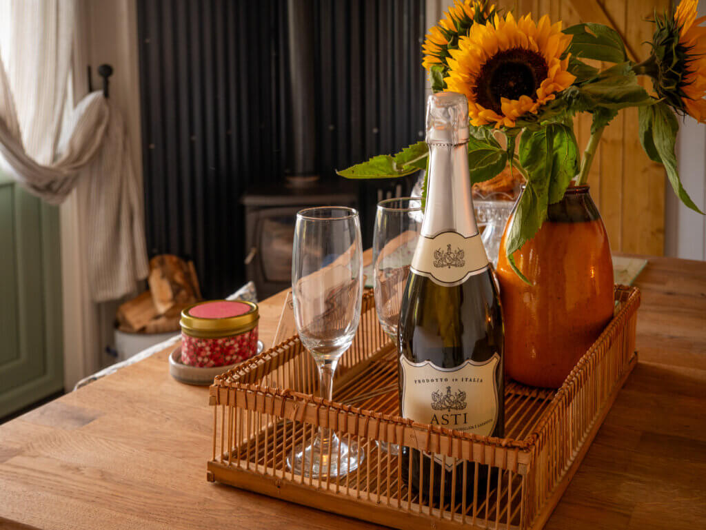 Bottle of Prosecco displayed on a table with two champagne glasses and a vase of sunflowers