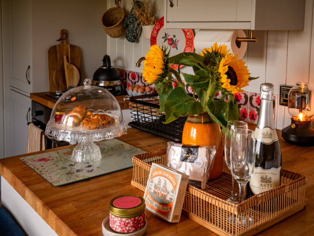 Table displaying a candle, vase of sunflowers, cake stand and a bottle of prosecco