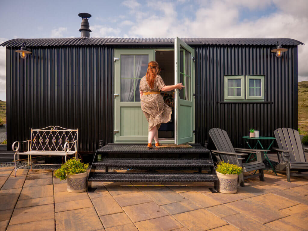 Woman wearing a brown dress entering a unique Shepherd's hut in Northern Ireland