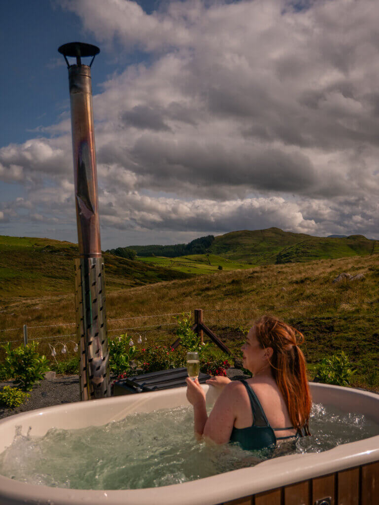 Woman in a wood burning hot tub holding a glass of champagne.