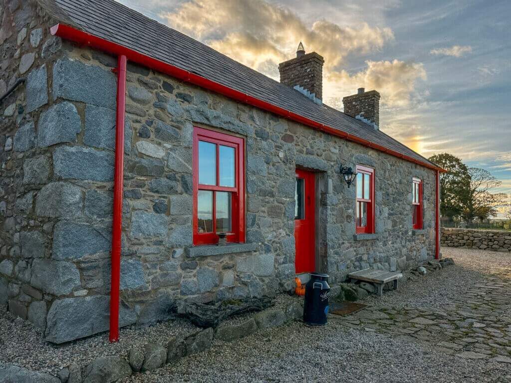 Stone cottage in Northern Ireland with red window frames and door.