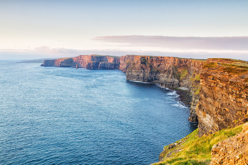Dramatic sunset over the Cliffs of Moher, casting long shadows and vibrant colours.