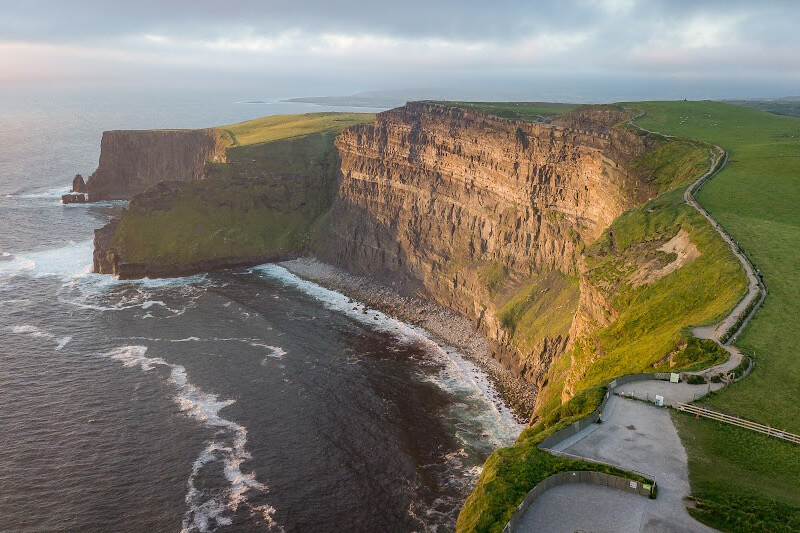 Panoramic views of lush green fields and a car park at the Cliffs of Moher in Ireland.