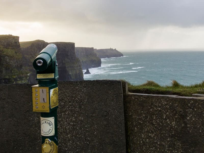 Experiencing the windswept freedom and breathtaking views at a lookout point, with telescope, from the top of the Cliffs of Moher, Ireland.