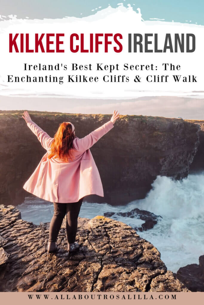 Image of Nicola Lavin, travel blogger standing at the edge of the Kilkee Cliffs. Her hands are raised and waves are crashing all around. There is text overlay Ireland's Best Kept Secret: The Enchanting Kilkee Cliffs & Cliff Walk.