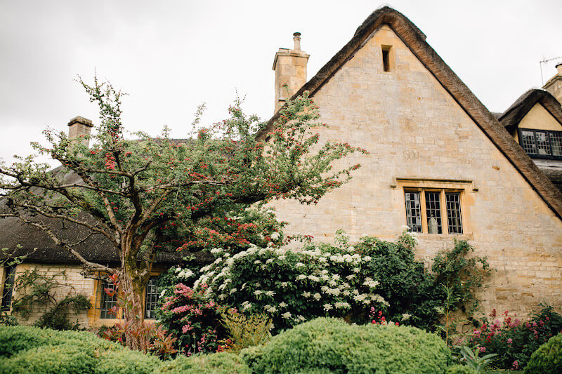 Picturesque thatched-roof cottage surrounded by colourful gardens in the Cotswolds.