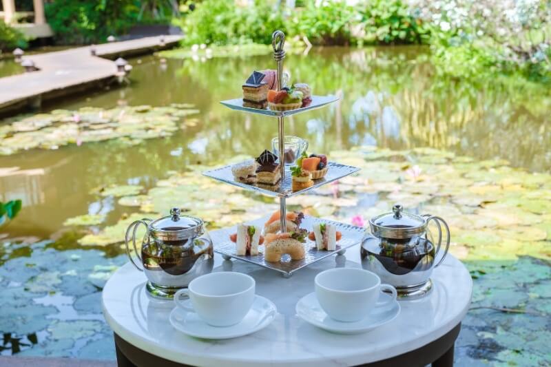 Luxury afternoon tea setting beside a pond in the Cotswolds countryside.