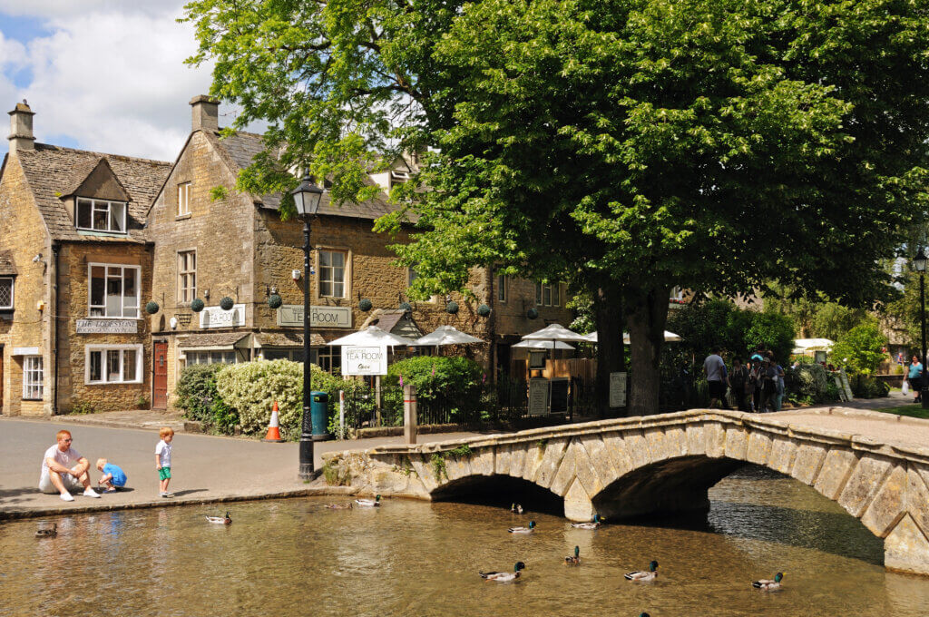 Bourton on the Water, United Kingdom:  Father with two children looking at the ducks on the River Windrush with tea-rooms to the rear, Bourton on the Water, Gloucestershire, England, UK, Western Europe.
