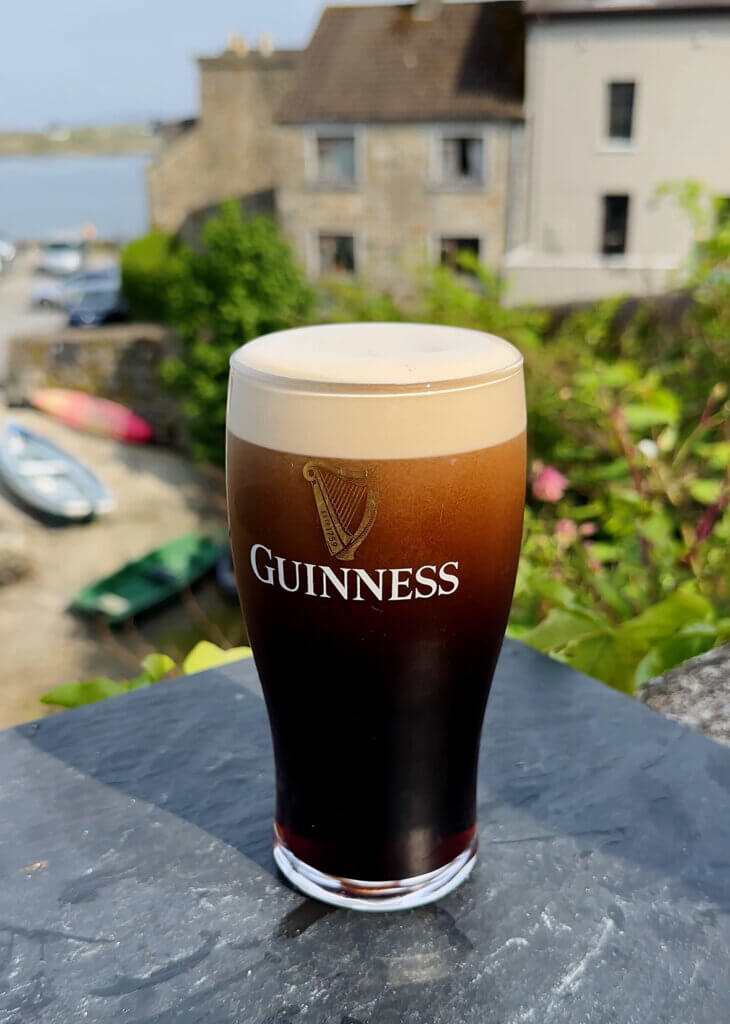 A pint of Guinness with the backdrop of Rounstone village, a charming fishing village in Connemara, Ireland.
