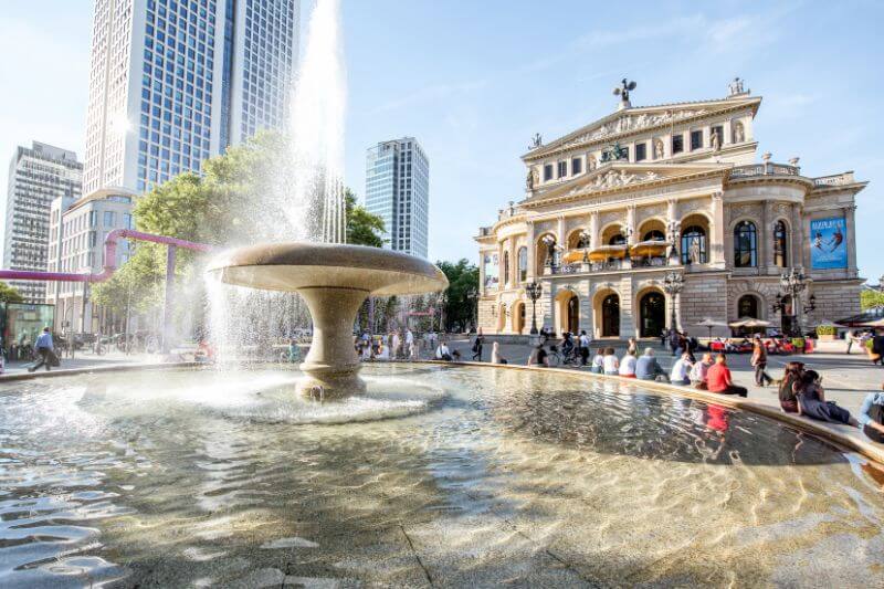 People sitting around a fountain in the centre of Frankfurt city on a sunny day.