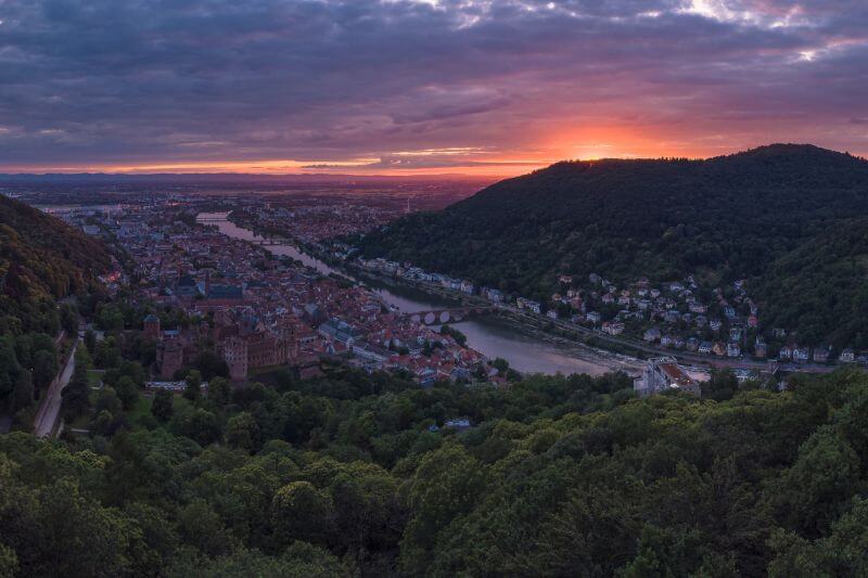 Sunset over Heidelberg, casting a warm glow on the Neckar River and surrounding hills.