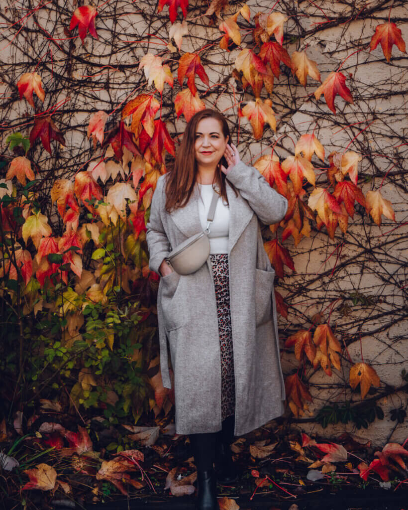 A woman wears a warm wool coat and stands beside autumn foliage in Ireland.