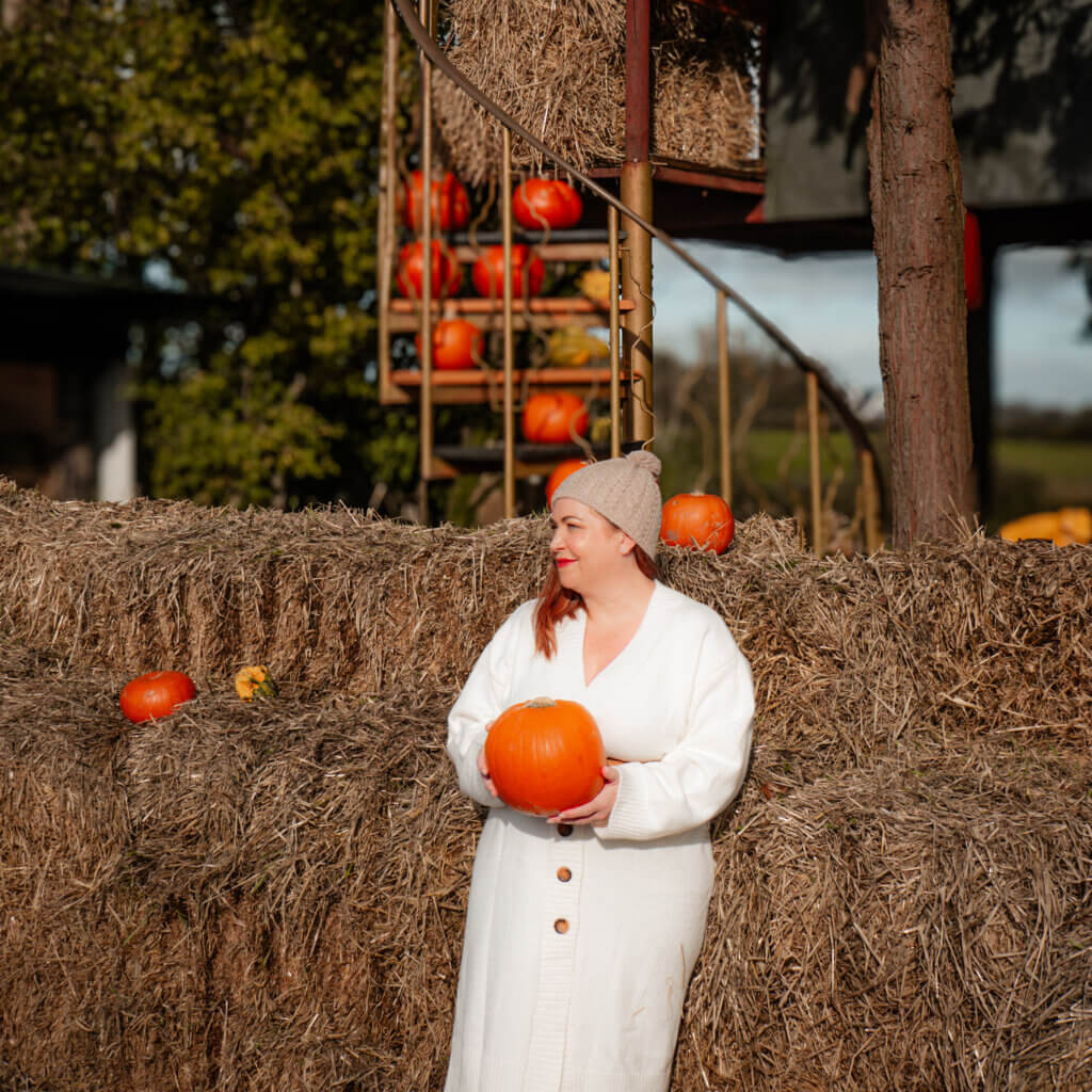 Nicola Lavin is an Irish Travel blogger. She is posing for a photo holding a pumpkin at Killarney Pumpkin Farm in Ireland.