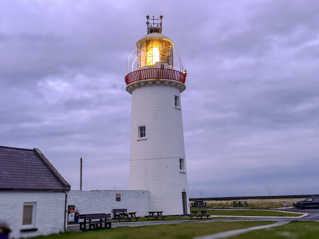 Loop Head Lighthouse lit up at dusk, with the last light of day fading away.