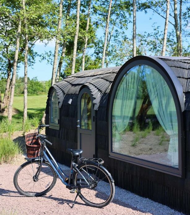 Exterior view of Ballygarry Estate’s luxury cabins in Ireland surrounded by trees and morning light. A blue bicycle with a rustic picnic basket is parked outside.